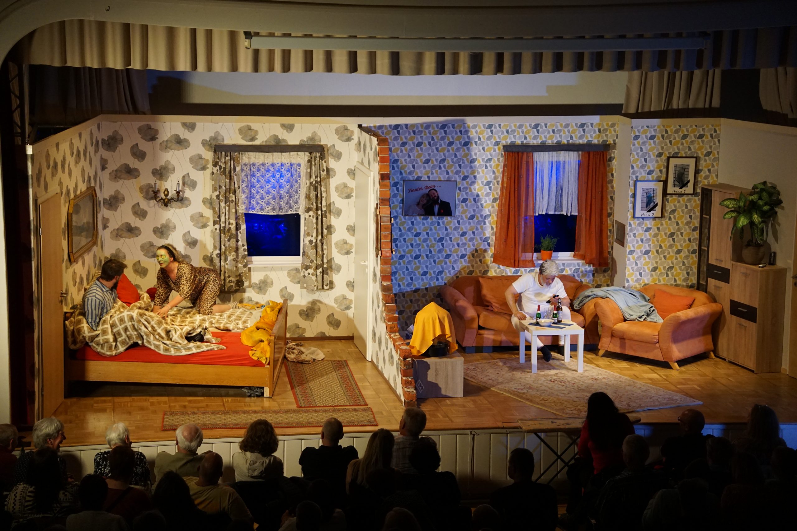 Szenenbild Mordgedanken: Die Bühne ist geteilt. Links ein Schlafzimmer, rechts ein Wohnzimmer. Im Schlafzimmer versucht Horst Hilfreich zu schlafen, während seine Frau mit Gurkenmaske im Bett umherkriecht. Im Wohnzimmer sieht Horsts Vater fern.